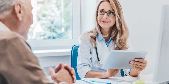 Middle aged female doctor nutritionist in white medical coat consulting her old patient using digital tablet