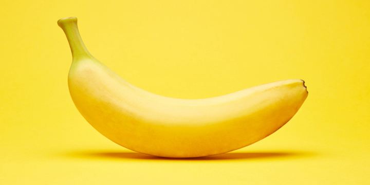 Single fresh raw clean isolated one alone horizontally oriented yellow banana on the bright solid yellow fond background bananas