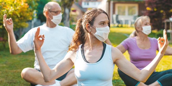 Multigenerational group of people making yoga exercises outdoors wearing medical protective masks yoga