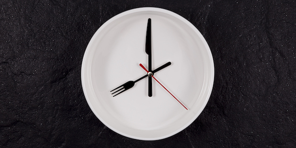 White plate clock on a dark textured stone background with copy space. The hands point to 8 o'clock. Concept - interval fasting or autophagy diabetes and intermittent fasting