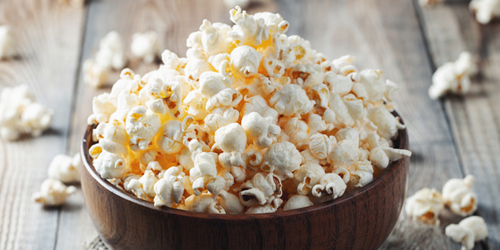 A wooden bowl of salted popcorn at the old wooden table. Dark background. selective focus popcorn