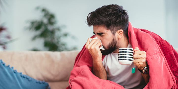 Man blowing his nose while lying sick in bed