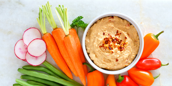 Hummus with fresh vegetables, above view on white marble