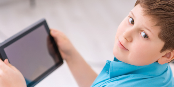 Chubby boy is busy with digital tablet Kid and tablet. Chubby boy is resting on the sofa and holding his portable tablet.
