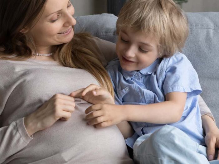 Cheerful expecting mom and little son hugging,