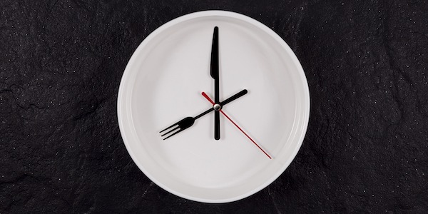 White plate clock on a dark textured stone background with copy space. The hands point to 8 o'clock. Concept - interval fasting or autophagy.