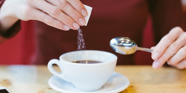 Woman's hands pouring sugar in black coffee - girl sitting at the table with espresso and smartphone - blood and glycemic index control for diabetes -excess of white sugar in food concept