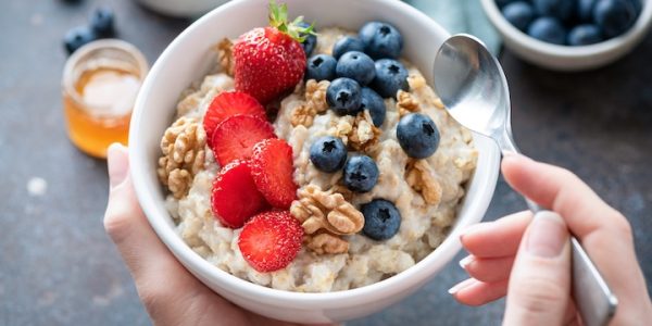 Oatmeal porridge bowl with berry fruits in female hands, closeup view. Healthy vegetarian breakfast food