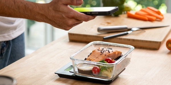 Man using phone while preparing healthy homemade meal prep with fresh food at home.