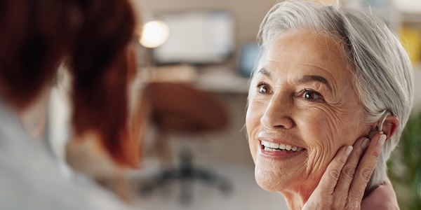 Doctor, senior woman and hearing aid in clinic for geriatric support, tinnitus and help for sound waves. Ent, otolaryngology and patient with cochlear implant for audio, healthcare and auditory tech