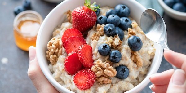 Oatmeal porridge bowl with berry fruits in female hands, closeup view. Healthy vegetarian breakfast food