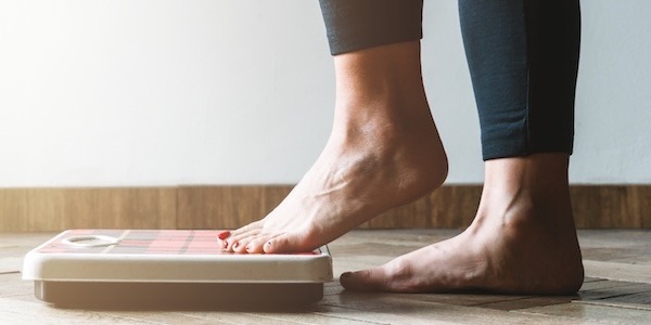 Female checking kilogrammes getting on the scale - self care and body positivity concept - warm flare on left Female checking kilogrammes getting on the scale - self care and body positivity concept - warm flare on left